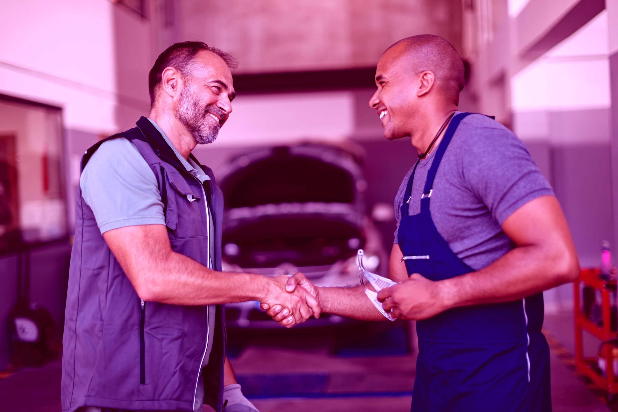 Happy mechanic greeting with his African American coworker at au